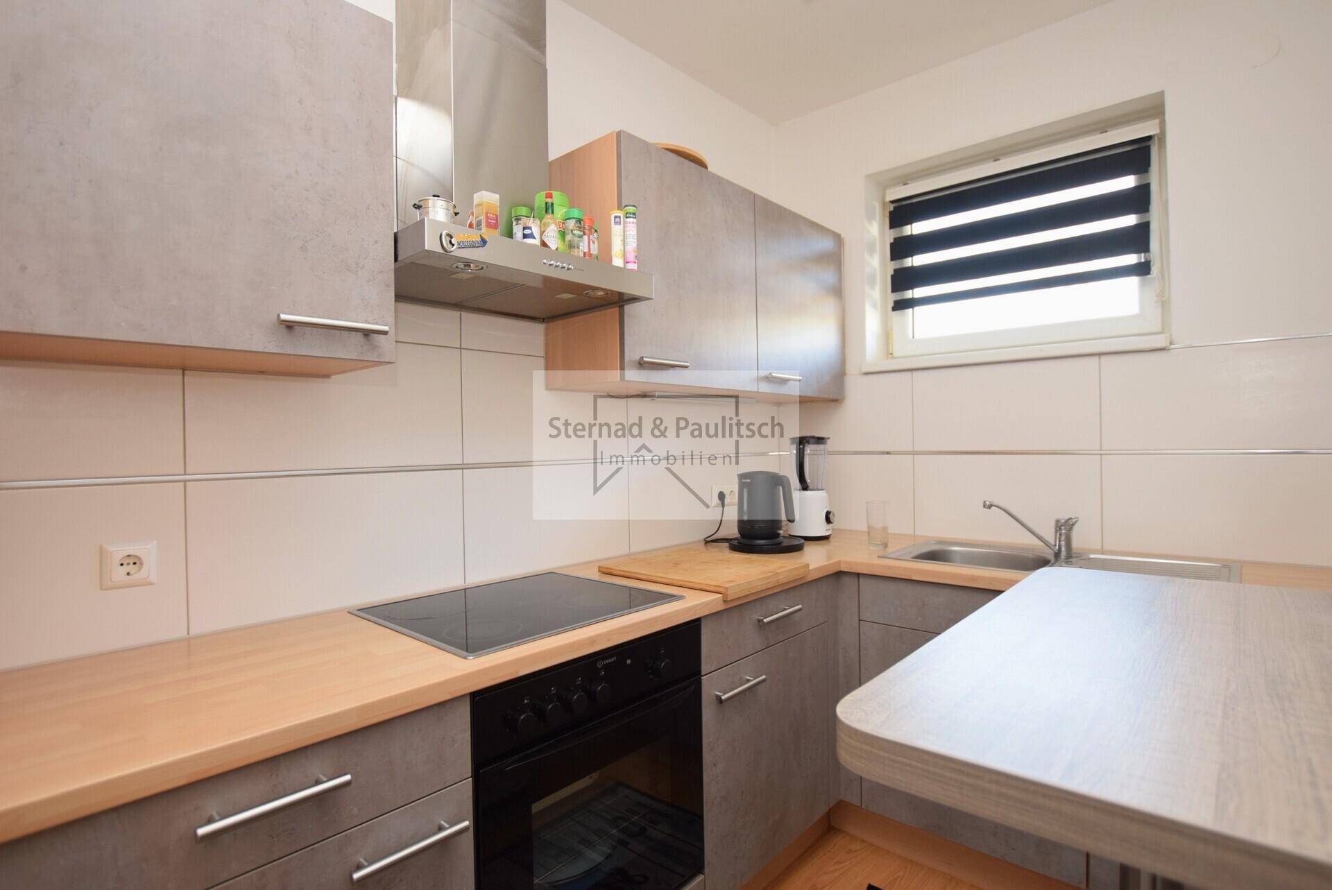 Funktionale Küche mit Induktionskochfeld, Backofen und Spüle unter dem Fenster.