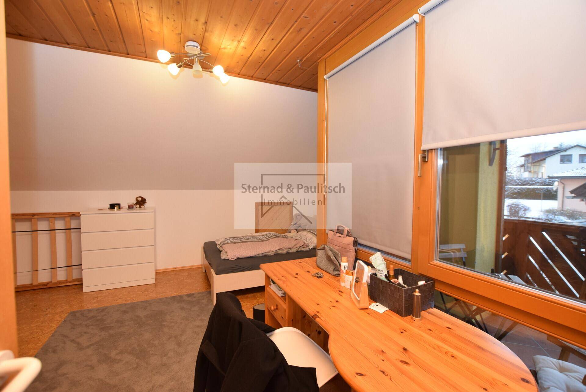 Schlafzimmer mit Dachschräge, Holzbalkendecke und Korkboden, hell und funktional eingerichtet.