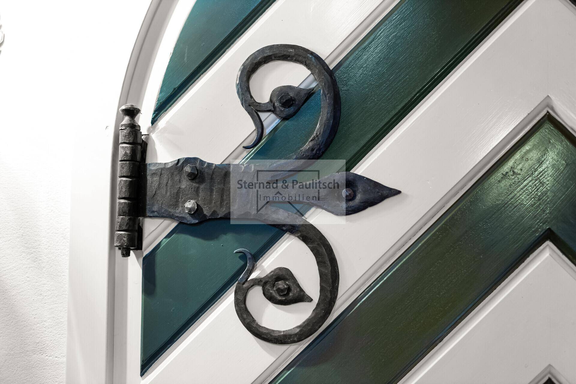 Nahaufnahme einer Tür mit grün-weißem Chevron-Muster und schmiedeeisernen Beschlägen.