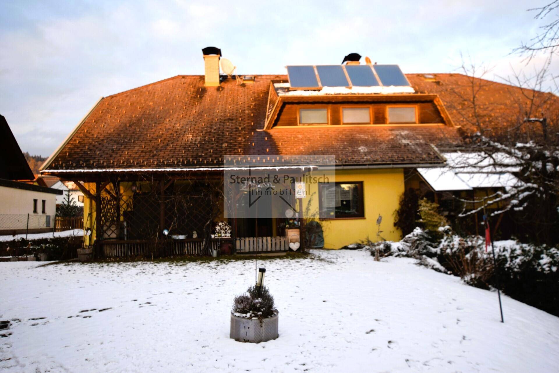Nahaufnahme des Hauses im Winter mit gelber Fassade, schneebedecktem Dach und Solarpaneelen.