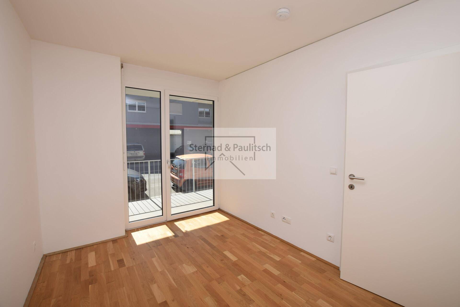 Helles Zimmer mit Parkettboden und großem Fenster, geeignet als Schlafzimmer oder Büro.