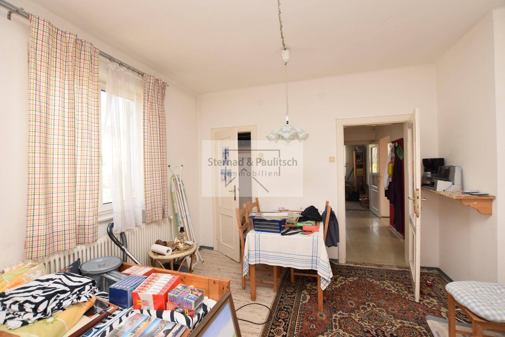 Zimmer mit Fenster, Tisch und Blick in den Flur.