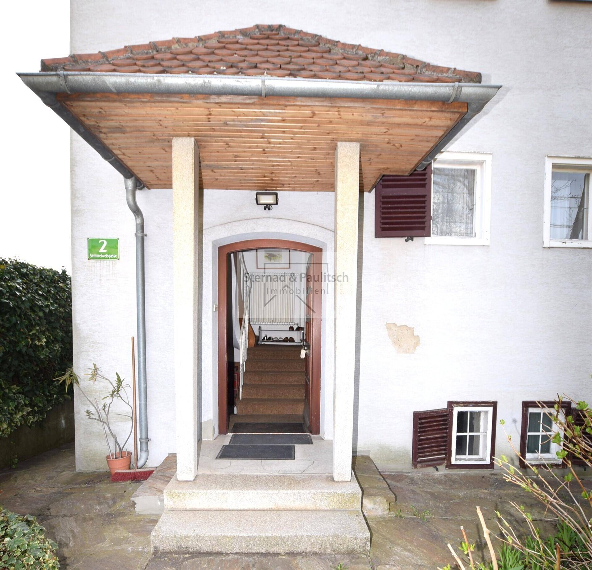 Überdachter Eingangsbereich des Hauses mit Treppe und Haustür.