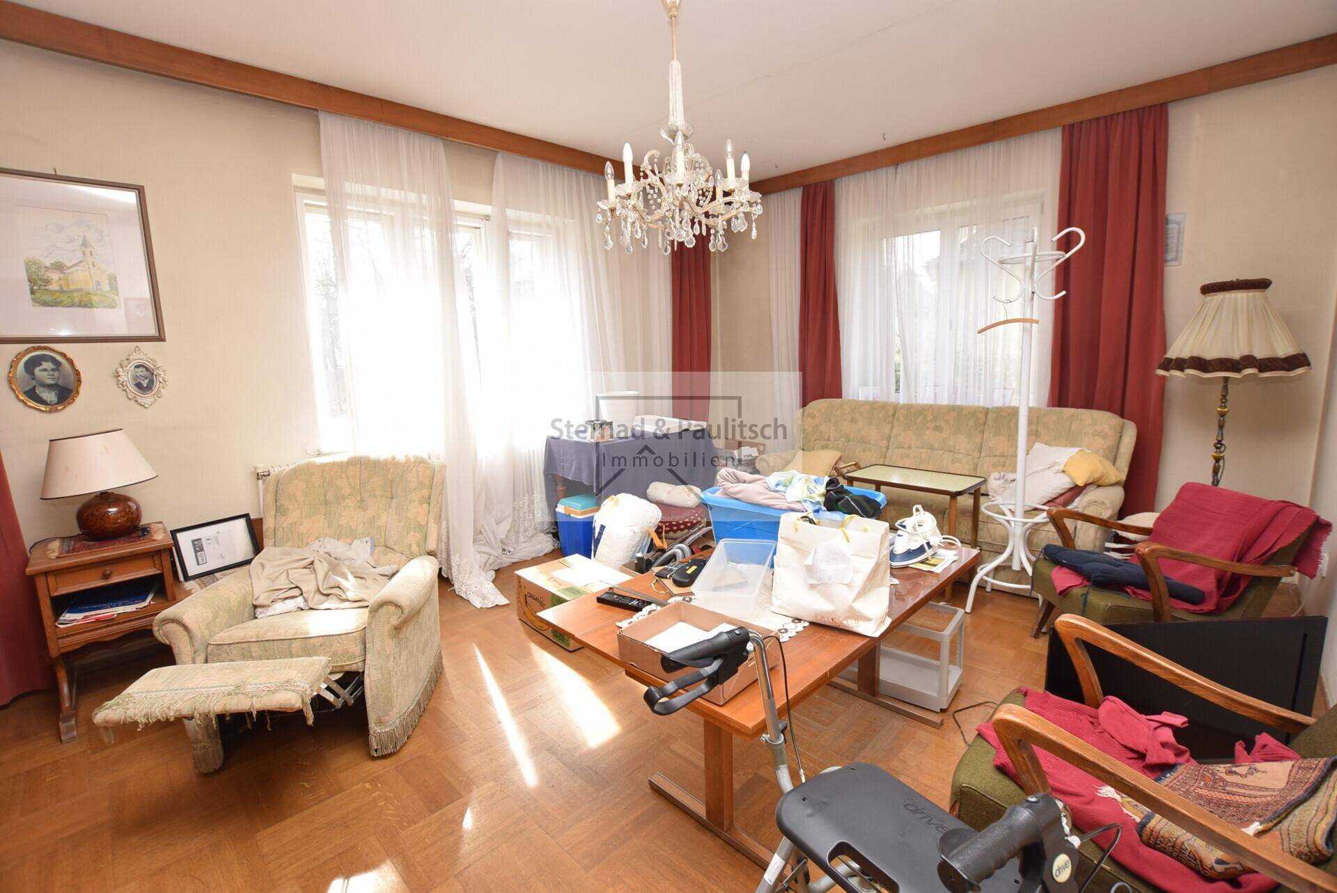Wohnzimmer mit Parkettboden, Kronleuchter und verschiedenen Möbelstücken.
