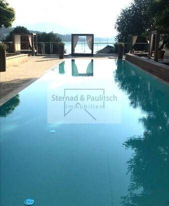 Blauer Swimmingpool mit eleganten Tagesbetten und weitem Blick auf den See.