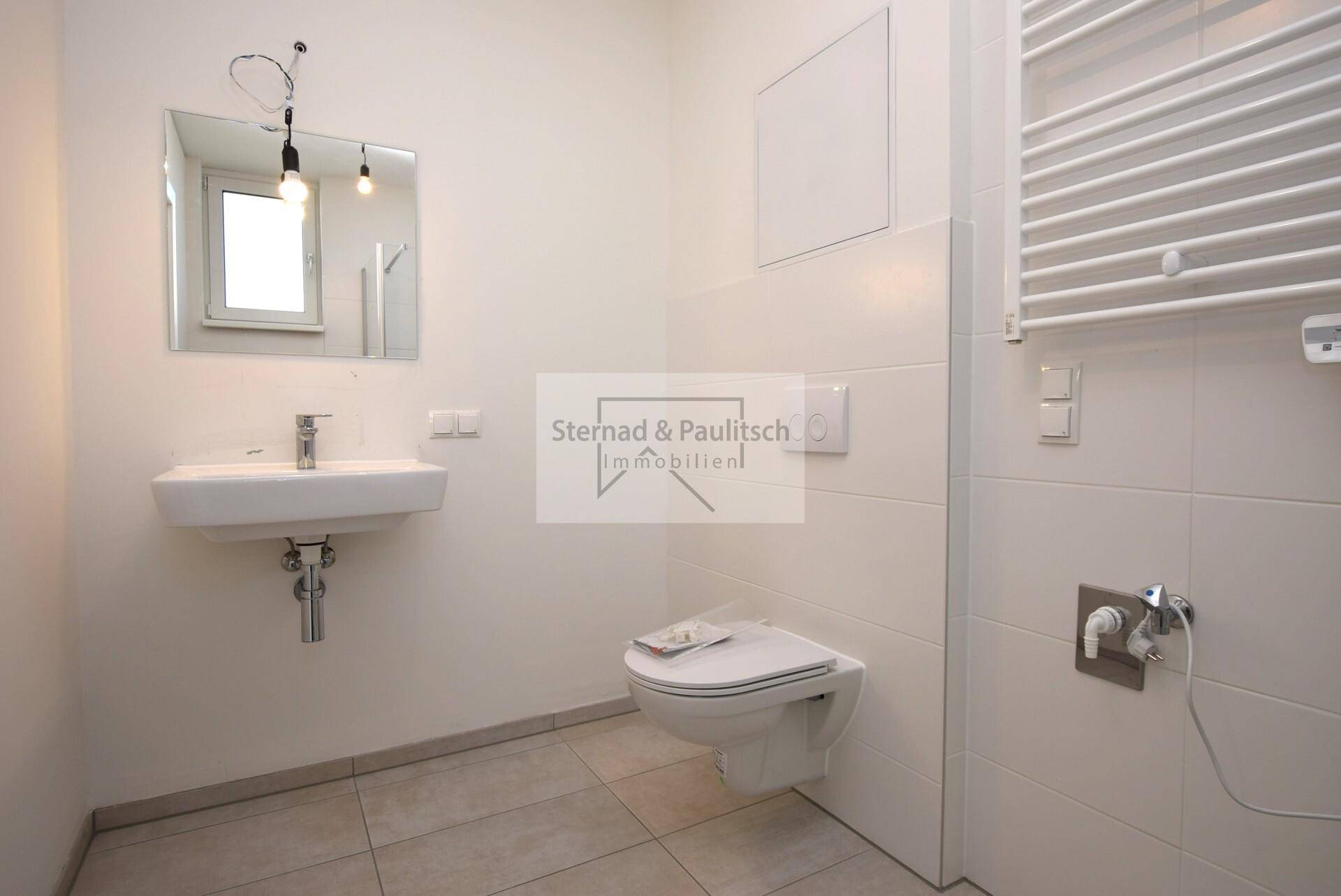 Helles Badezimmer mit wandhängendem WC, Einzelwaschbecken und Fenster, modern gefliest.
