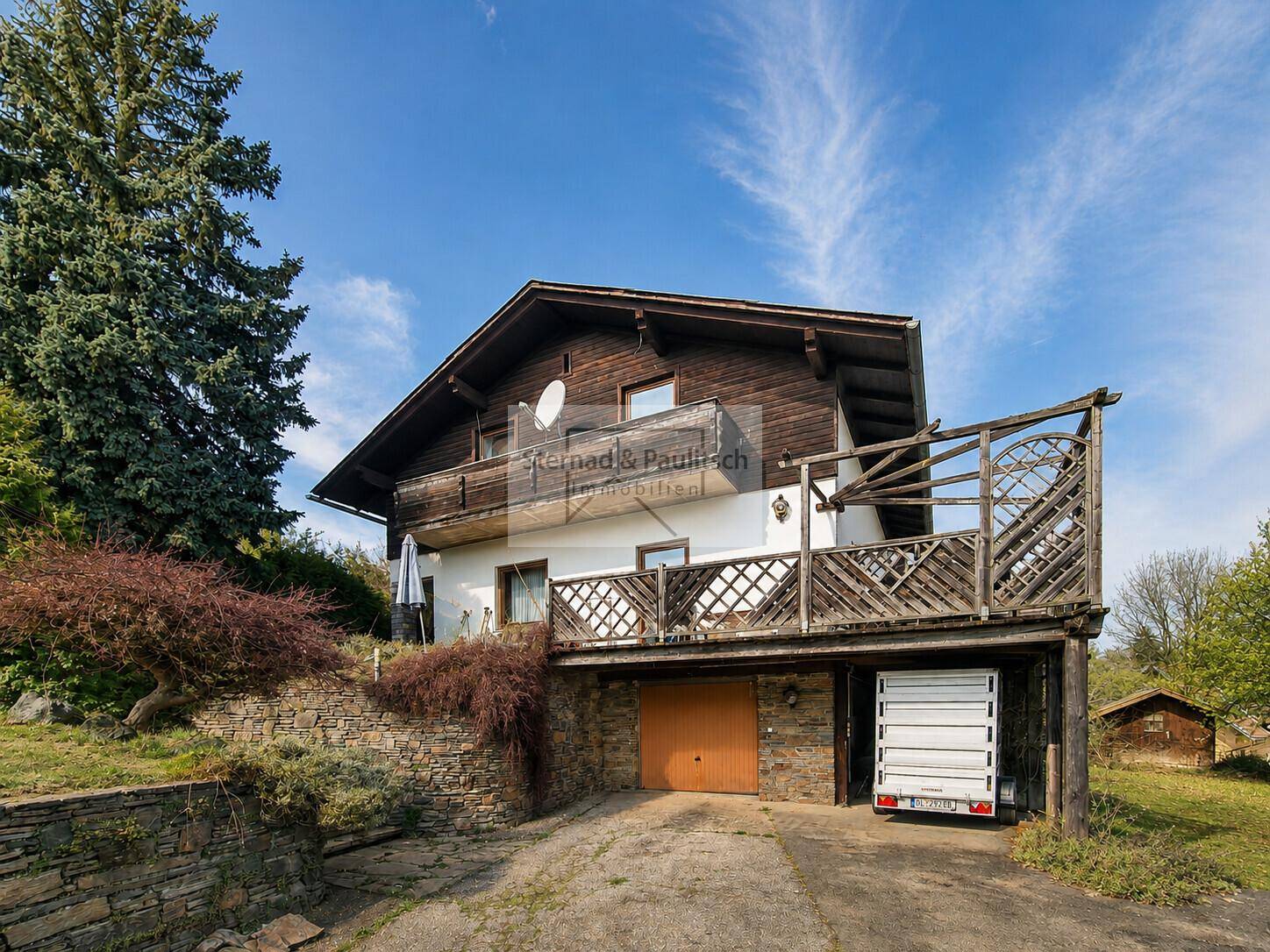 Ansicht des Hauses mit Garage im Untergeschoss und Holzverkleidung im Obergeschoss.