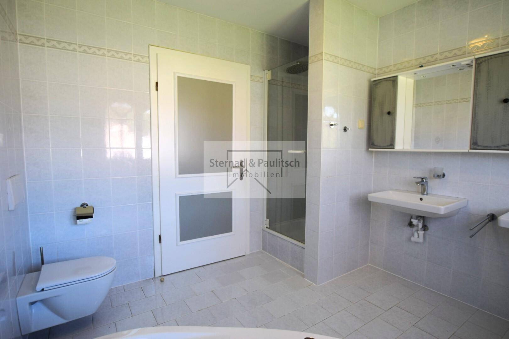 Badezimmer mit WC, Dusche und hellen Fliesen, funktional und gut gepflegt.