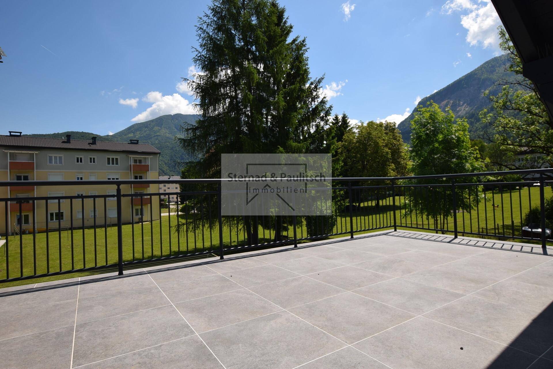 Großer Balkon mit Fliesenboden und Bergblick unter strahlend blauem Himmel.