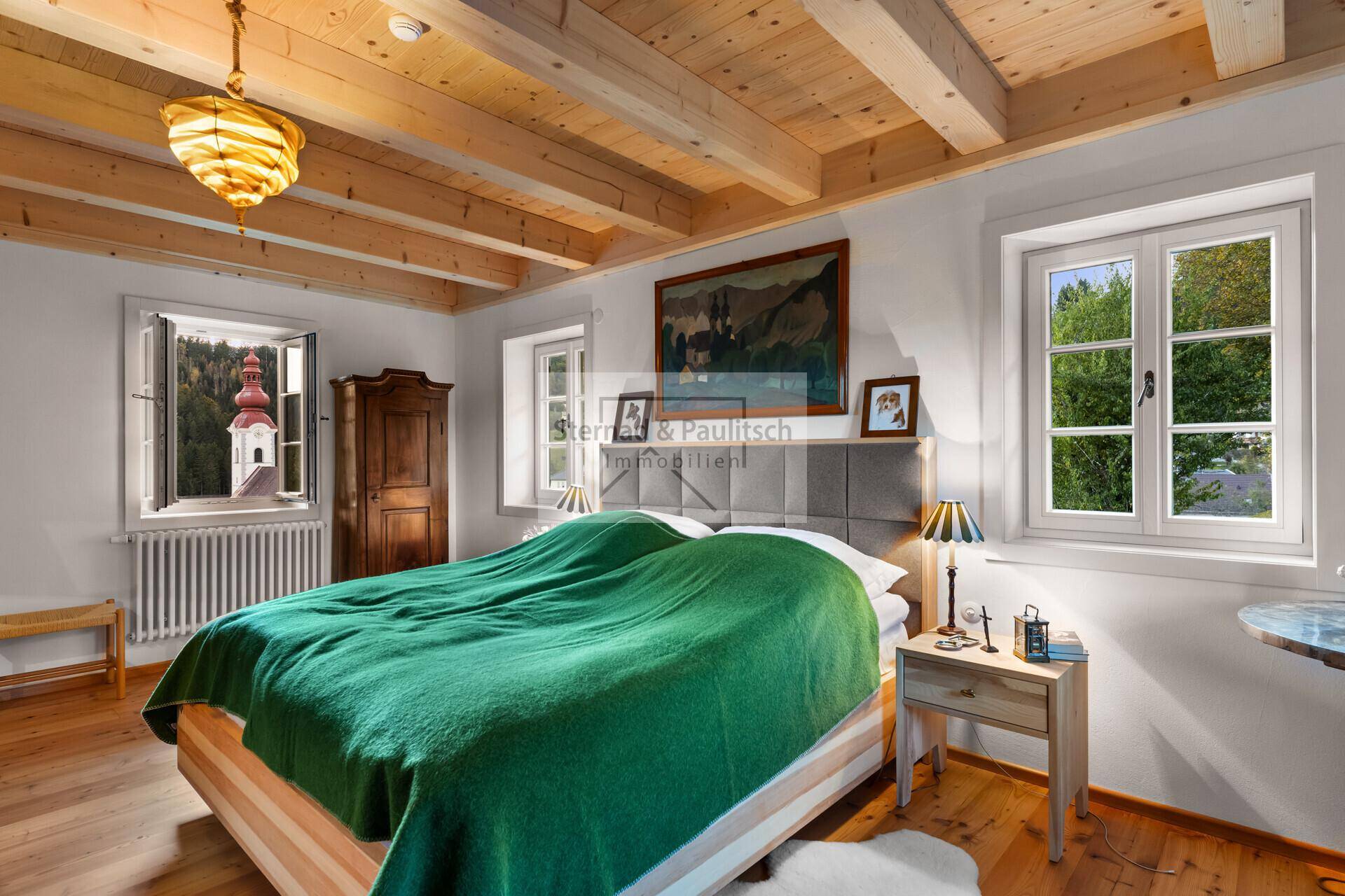 Gemütliches Schlafzimmer mit Holzbalkendecke, Holzboden und Fenstern mit Ausblick.
