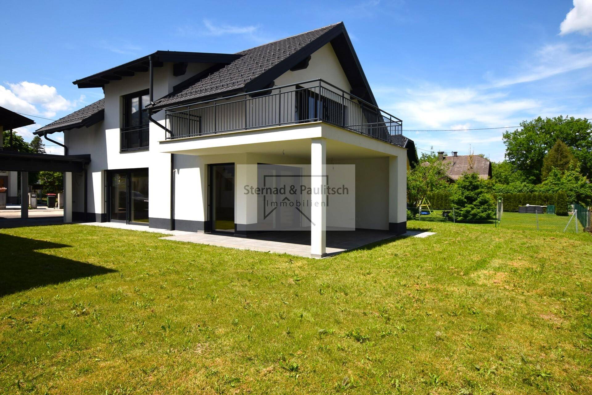 Freistehendes Haus mit gepflegtem Rasen und überdachter Terrasse im Sonnenschein.