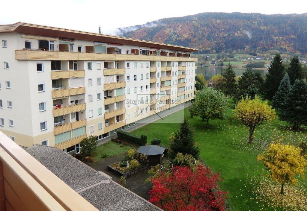 Mehrstöckiges Apartmentgebäude mit Balkonen, umgeben von einem gepflegten Garten und Seeblick.