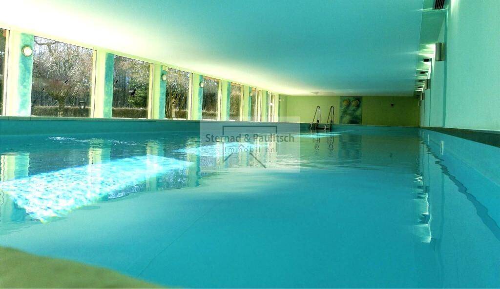 Großes Hallenbad mit viel Tageslicht durch die Fensterfront und hellgrünen Wänden, einladend zum Schwimmen.