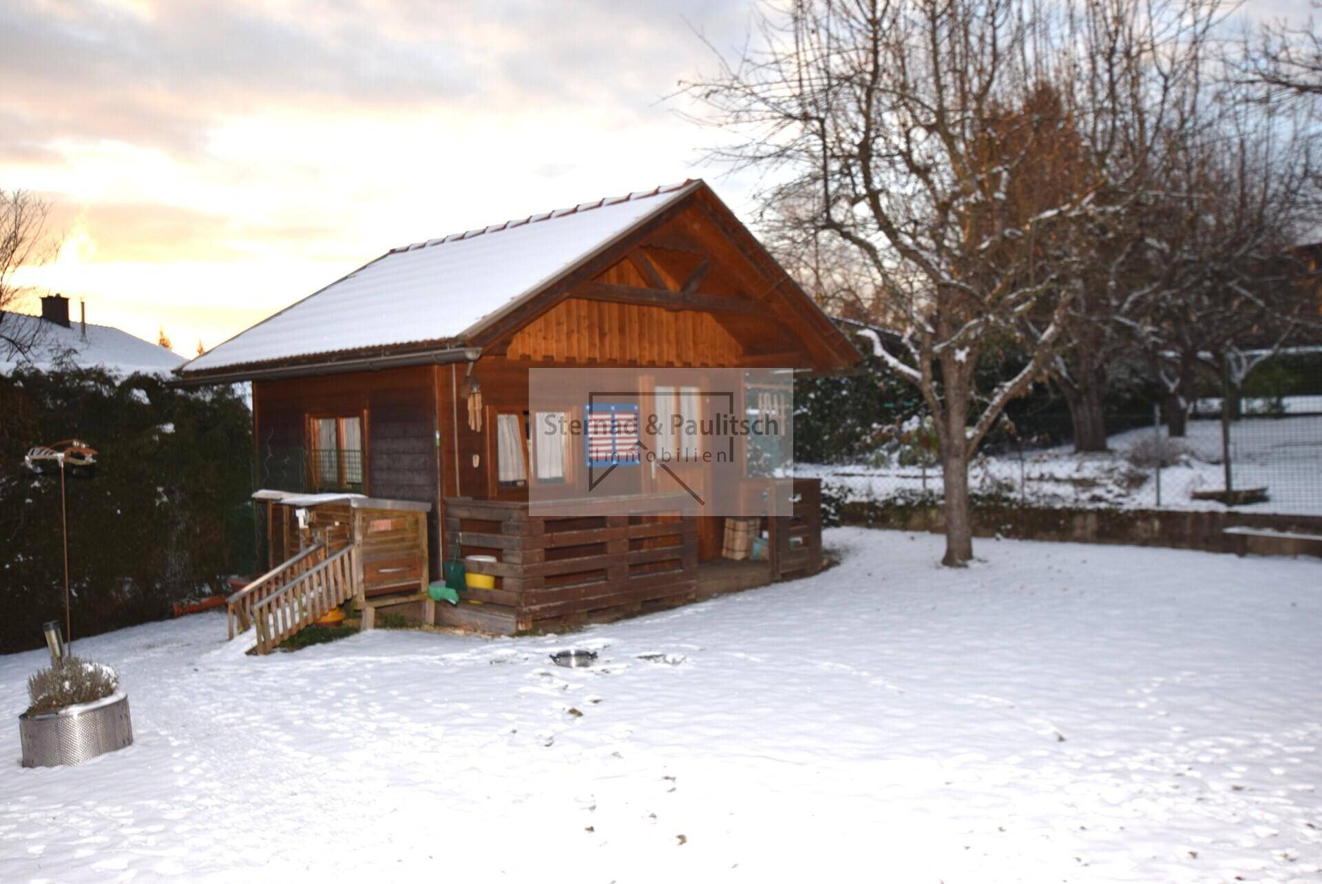 Kleines Gartenhaus aus Holz im verschneiten Garten.