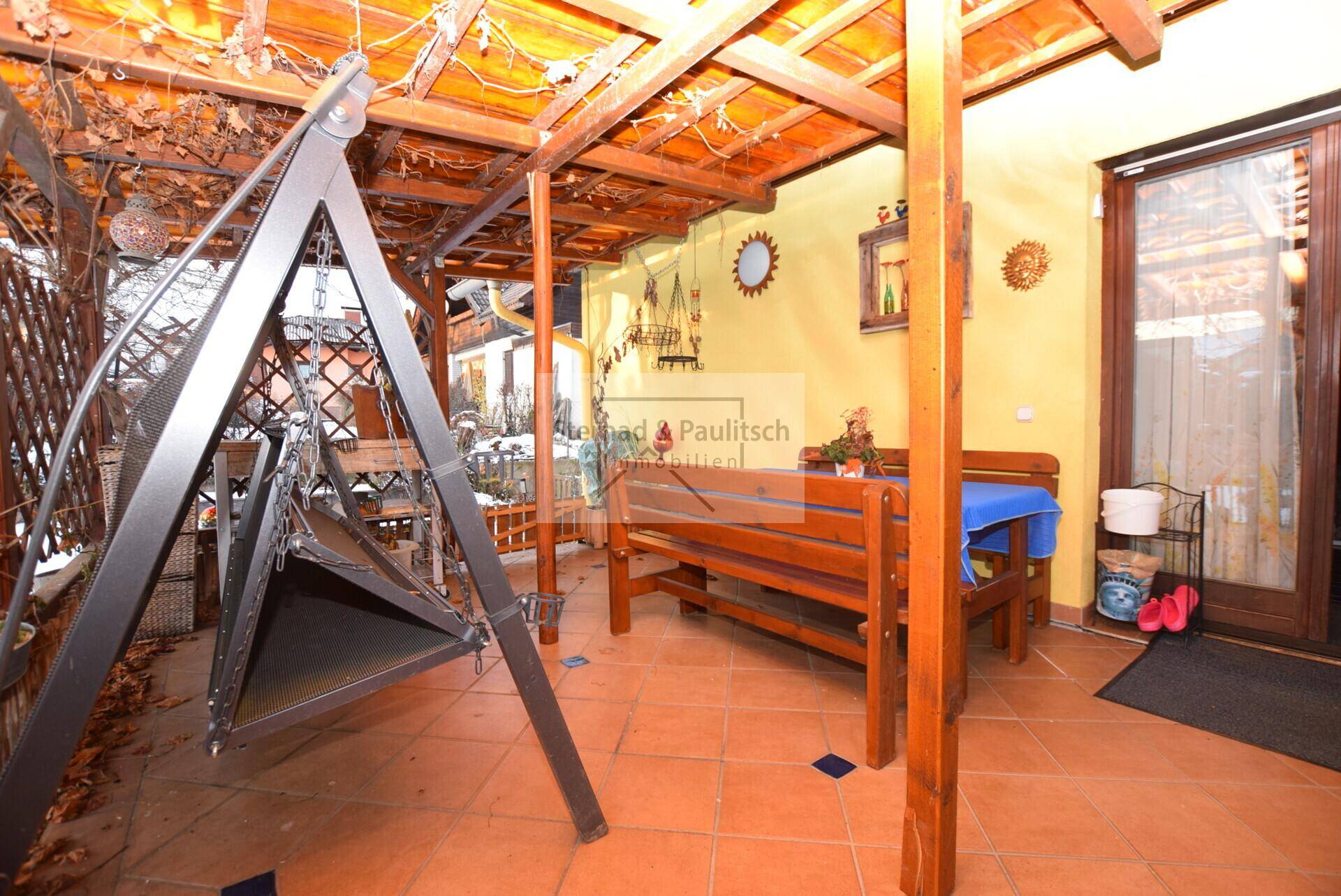 Überdachte Terrasse mit Holzbalken, Fliesenboden und rustikalen Sitzgelegenheiten, ideal für draußen.