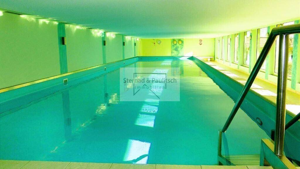 Großes, helles Hallenbad mit türkisfarbenem Wasser und großen Fenstern, ideal für Sport.