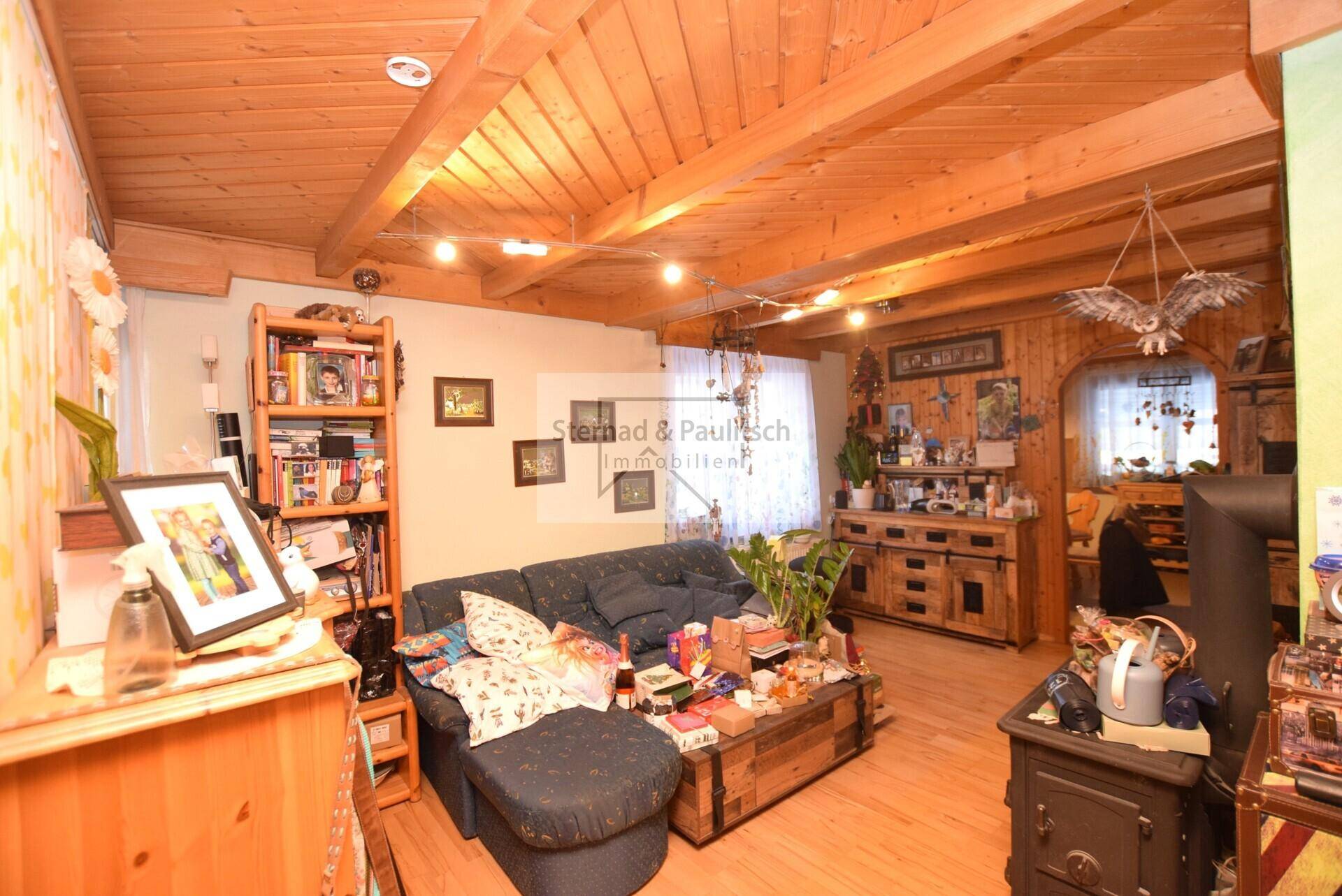 Rustikales Wohnzimmer mit Holzbalkendecke, Kaminofen und gemütlicher Sitzecke.