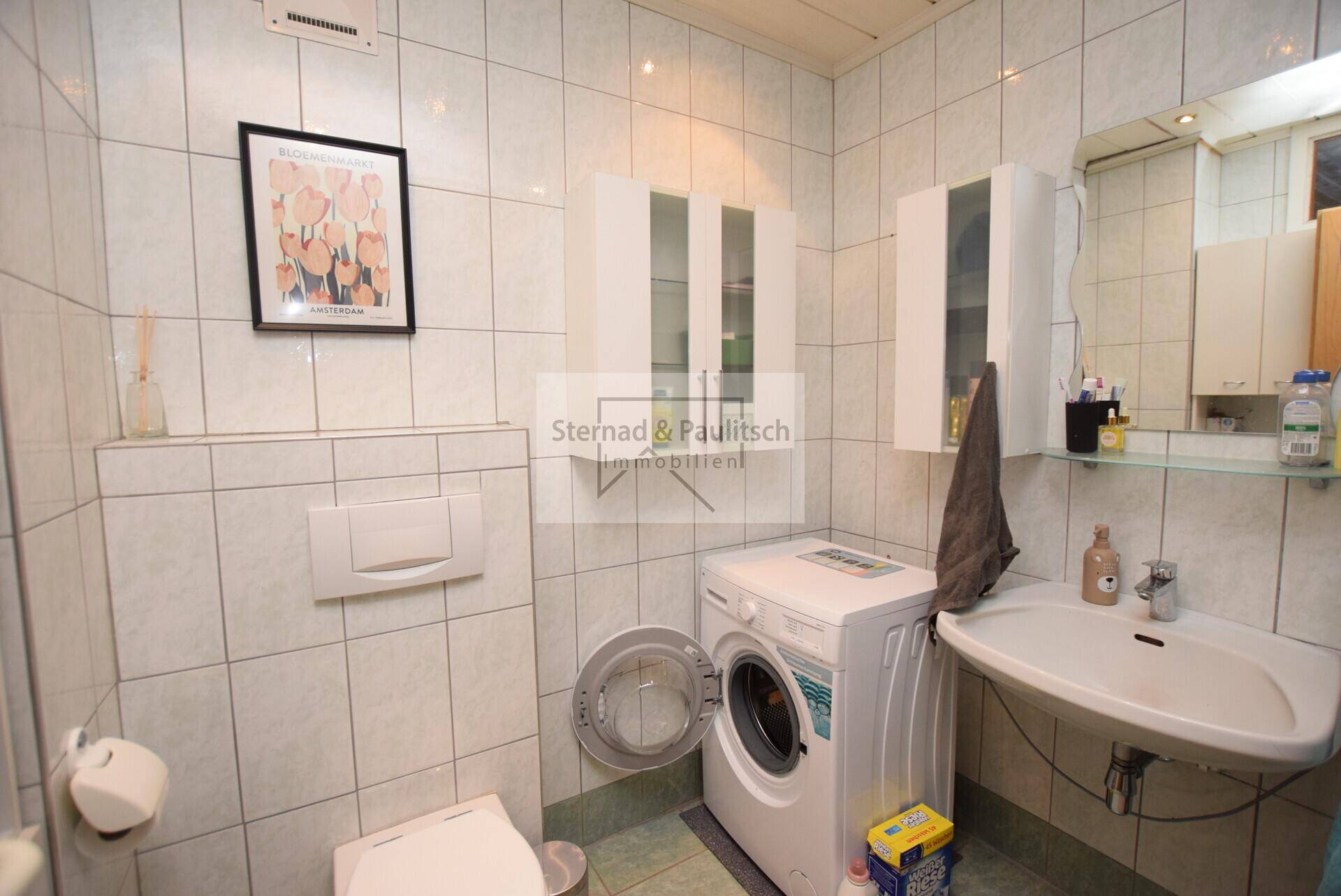 Badezimmer mit Waschmaschine, WC und hellen Fliesen.