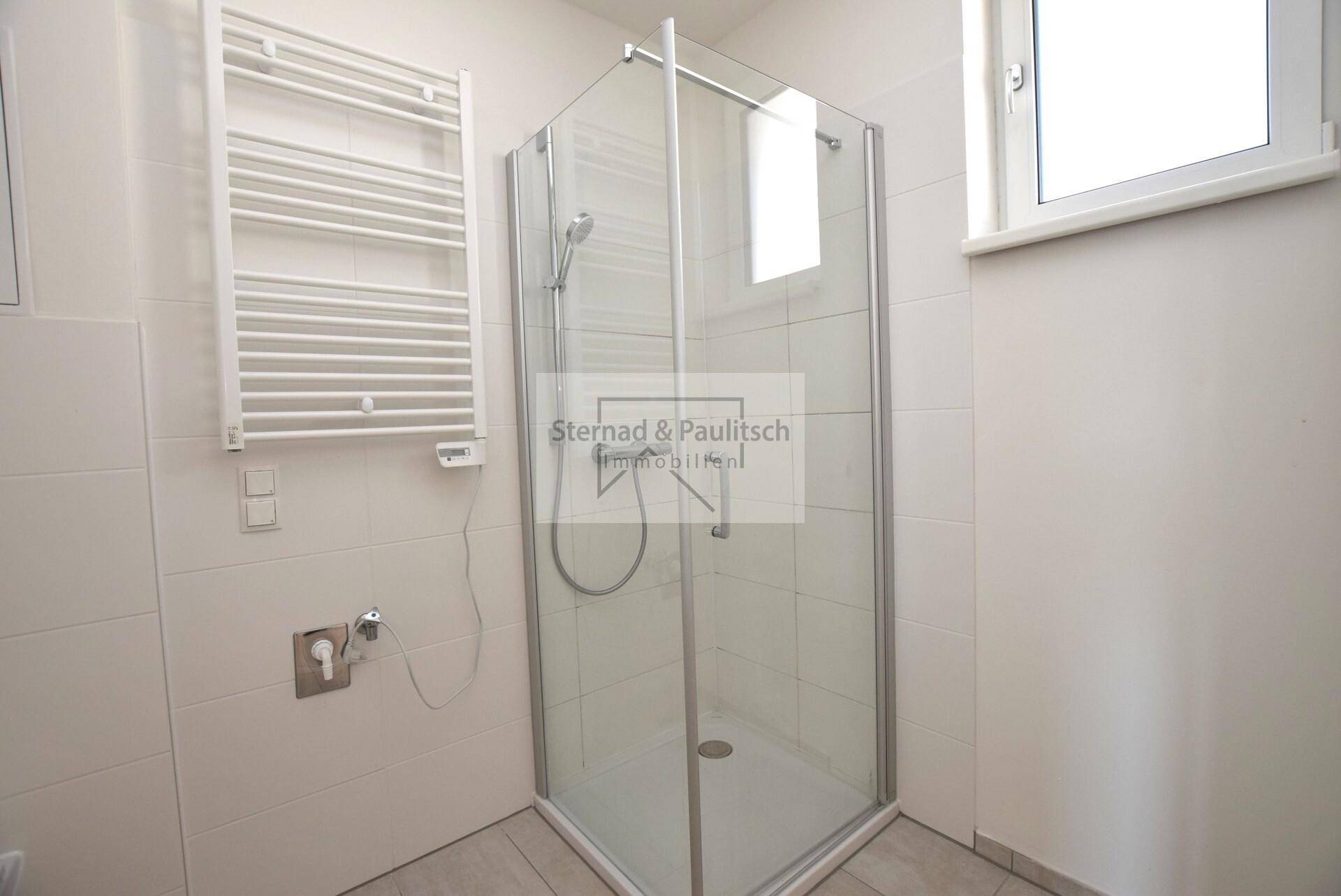 Modernes Badezimmer mit Duschkabine, Fliesenboden und beheiztem Handtuchhalter, hell und funktional.
