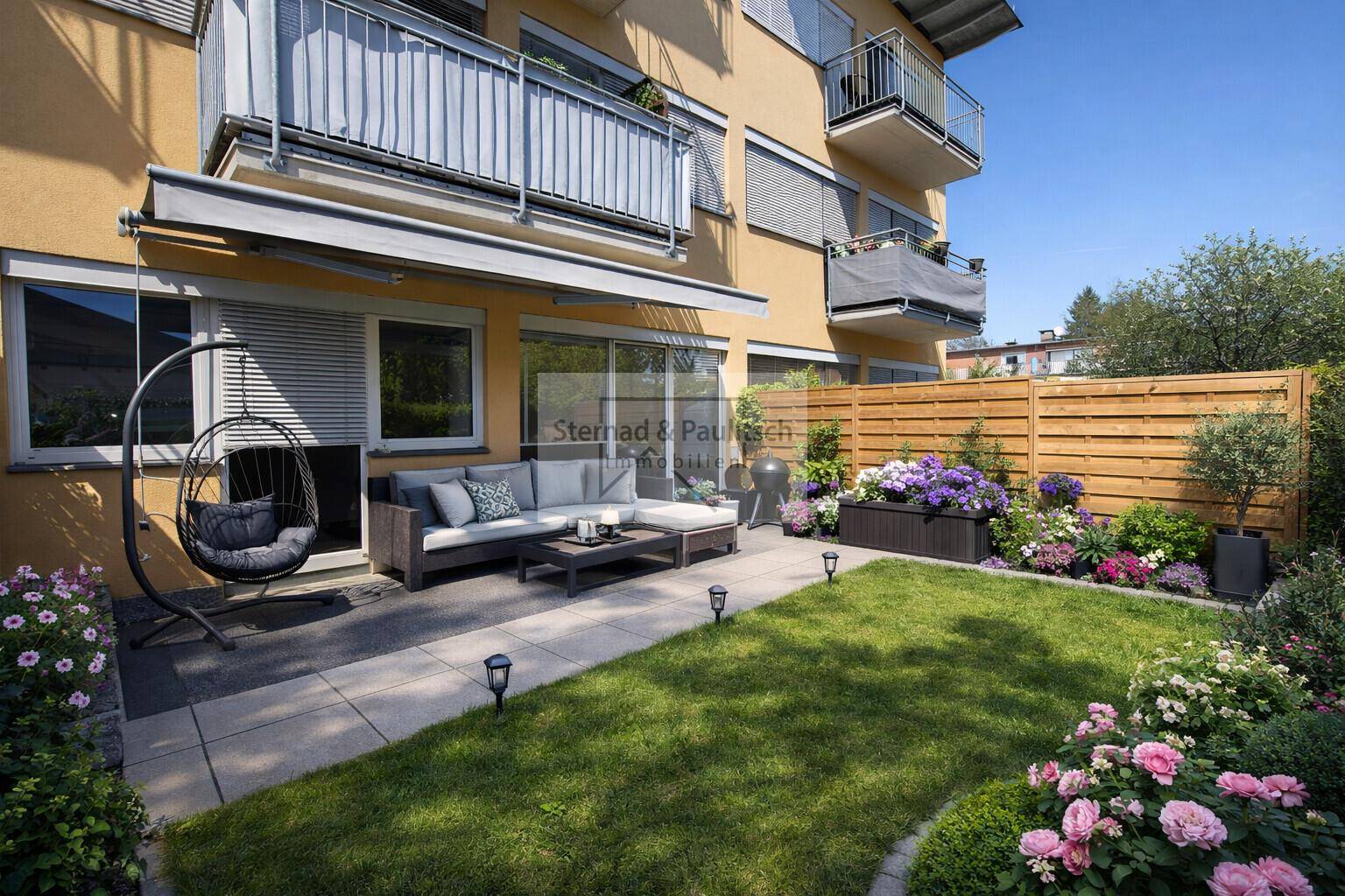 Gepflegter Garten mit möblierter Terrasse, Blumenbeeten und Holzzaun.