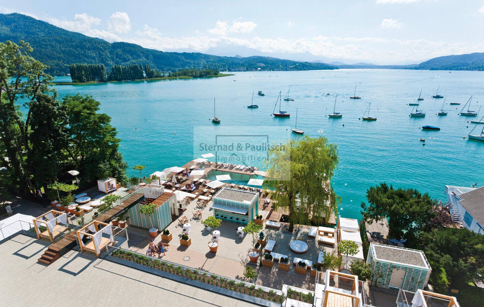 Beeindruckende Luftaufnahme einer weitläufigen Seeterrasse mit Pools und Liegebereichen vor Bergkulisse.