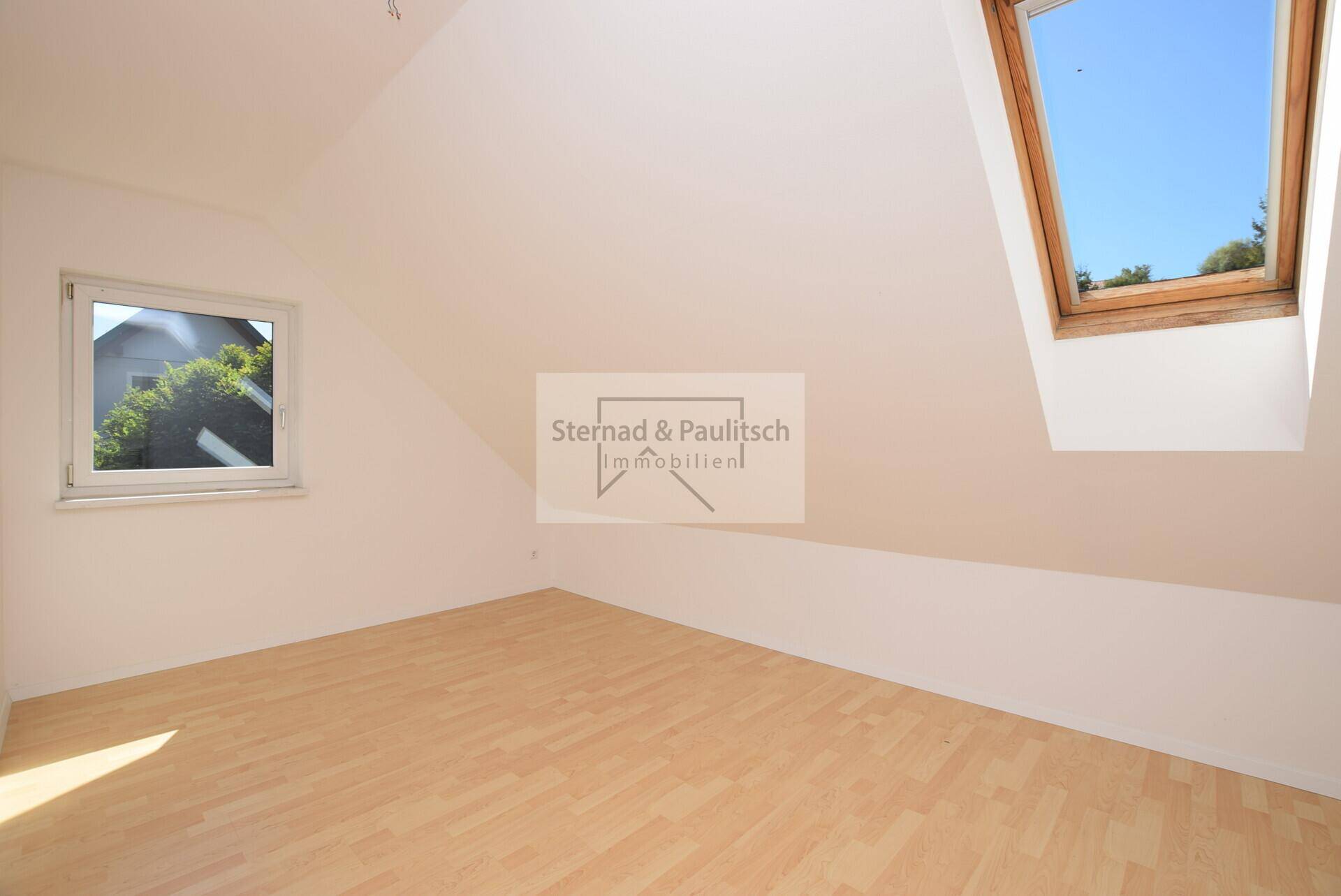 Helles Zimmer im Dachgeschoss mit Holzboden, Dachfenster und schrägen Wänden.