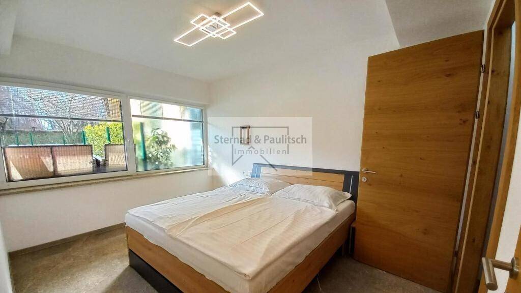 Schlafzimmer mit Doppelbett, großen Fenstern und Blick ins Grüne, hell und freundlich gestaltet.