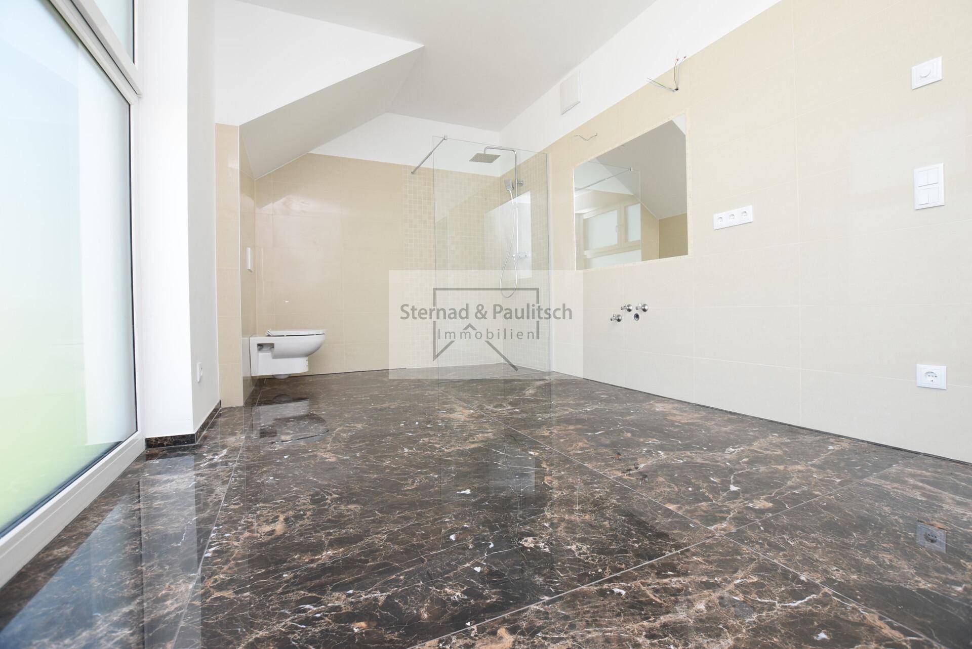 Geräumiges, unmöbliertes Badezimmer mit dunklen Fliesen, Dachschräge und Platz für eine Badewanne.