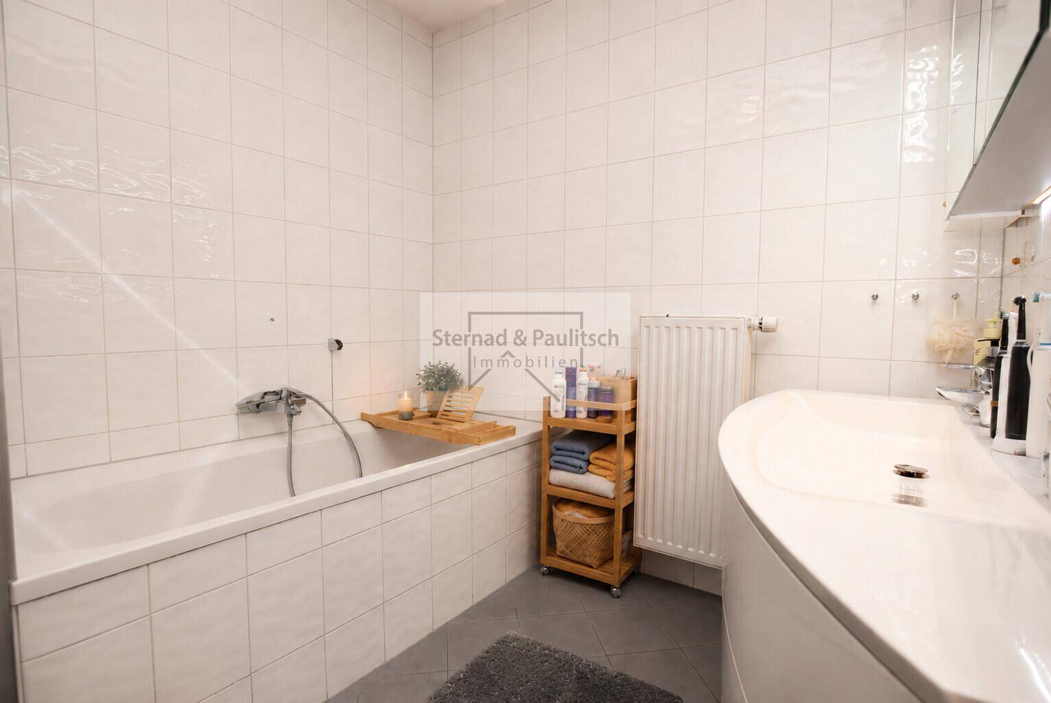 Helles Badezimmer mit Badewanne und modernem Waschbecken, komplett gefliest und gut gepflegt.