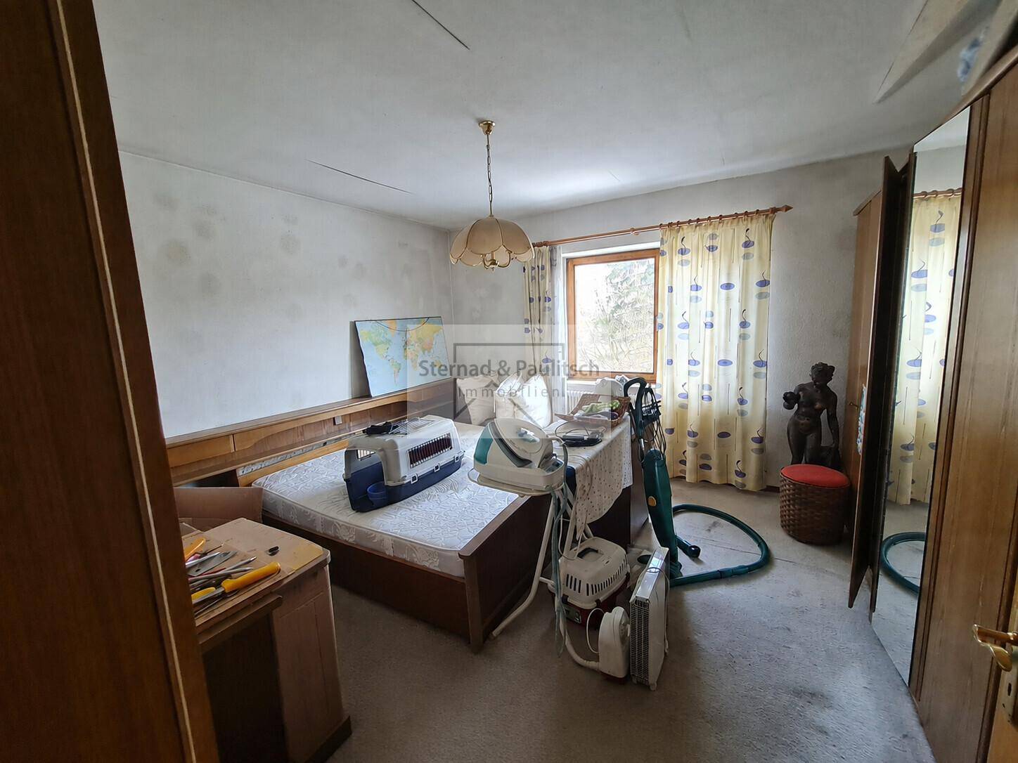 Schlafzimmer mit Bett, Kleiderschrank und Fenster, das eine Renovierung benötigt.