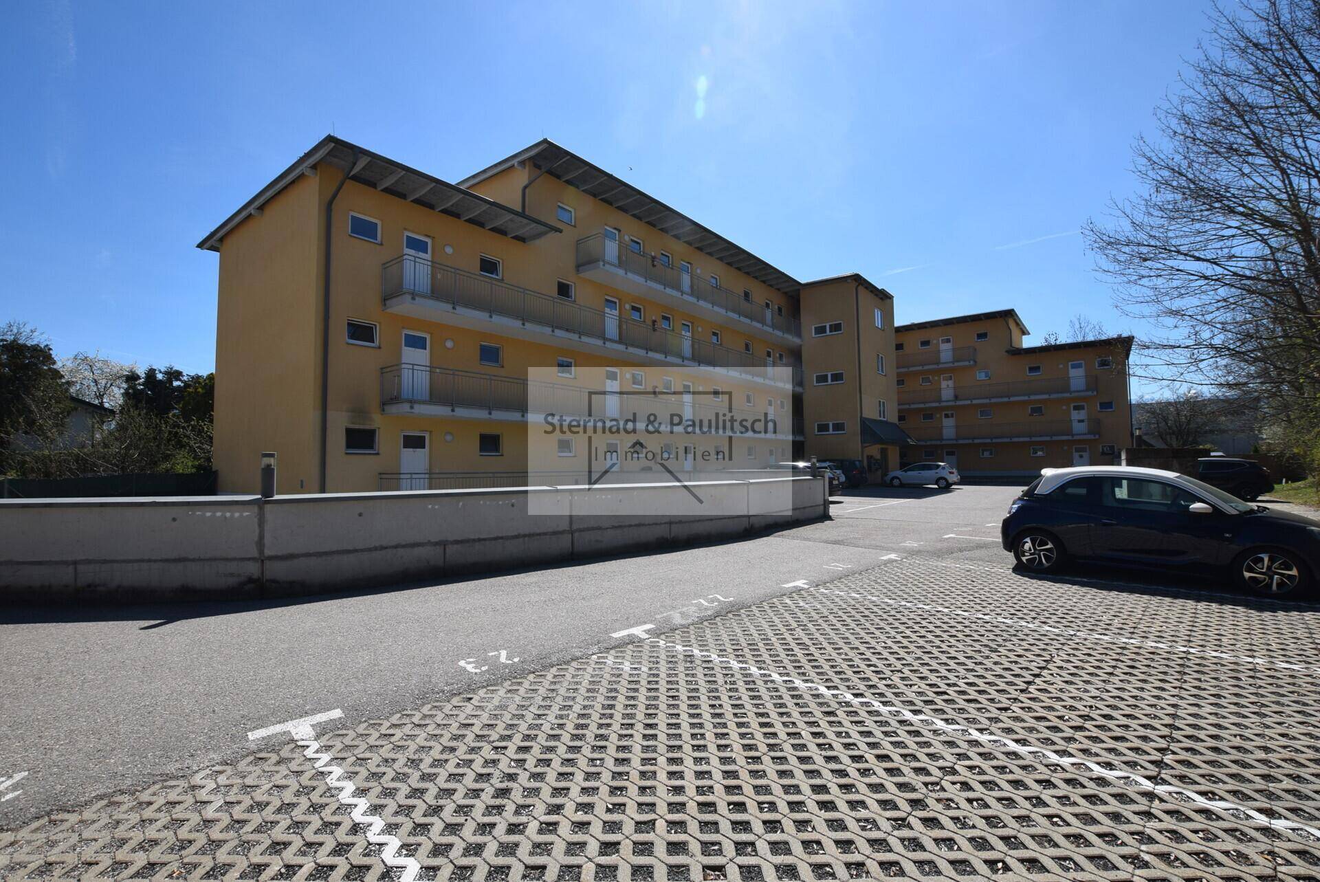 Wohngebäude mit gelber Fassade, Balkonen und großem Parkplatzbereich.