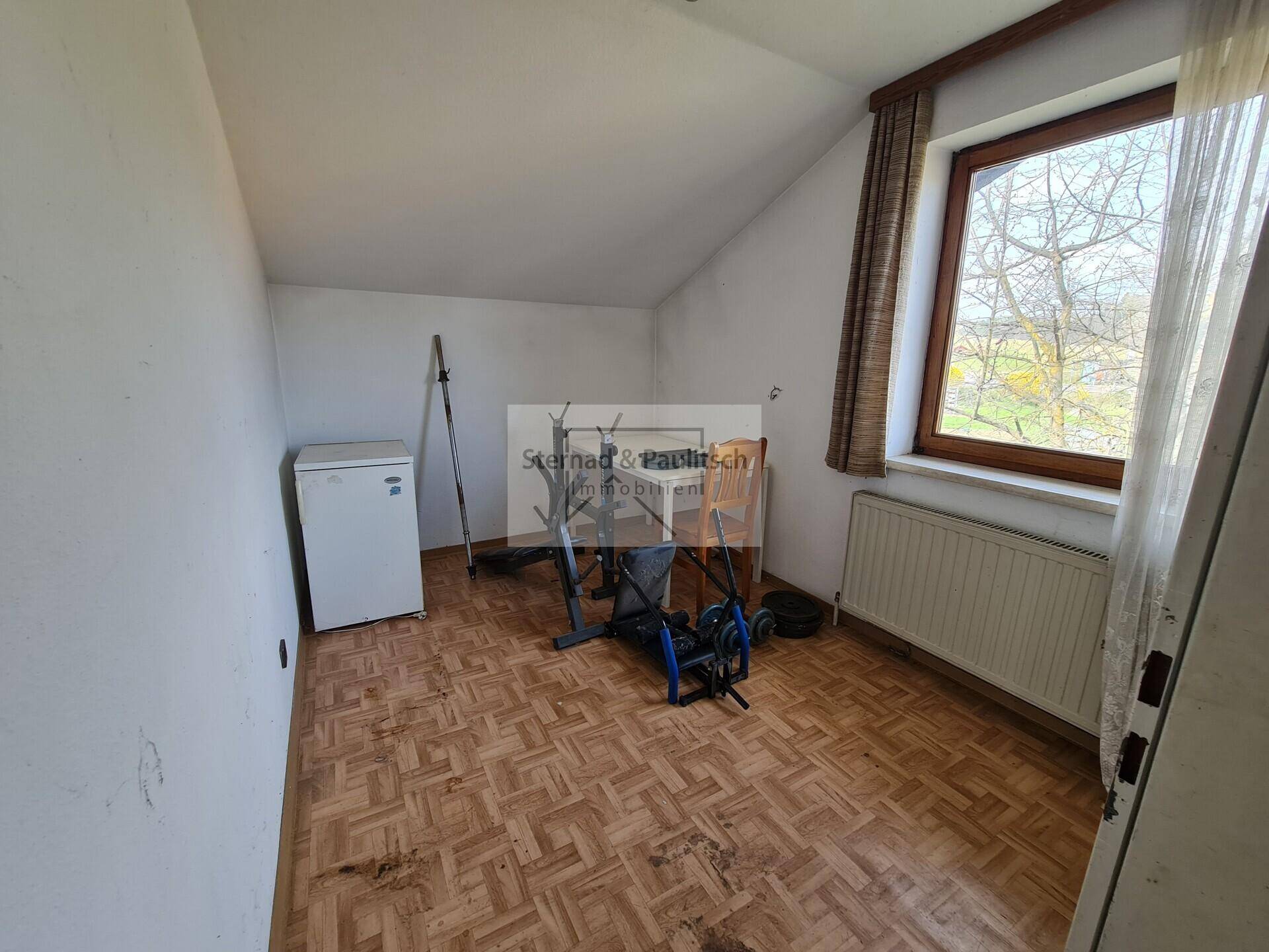 Kleiner Raum mit Dachschräge, Fenster und einfacher Ausstattung, möglicherweise als Gästezimmer nutzbar.