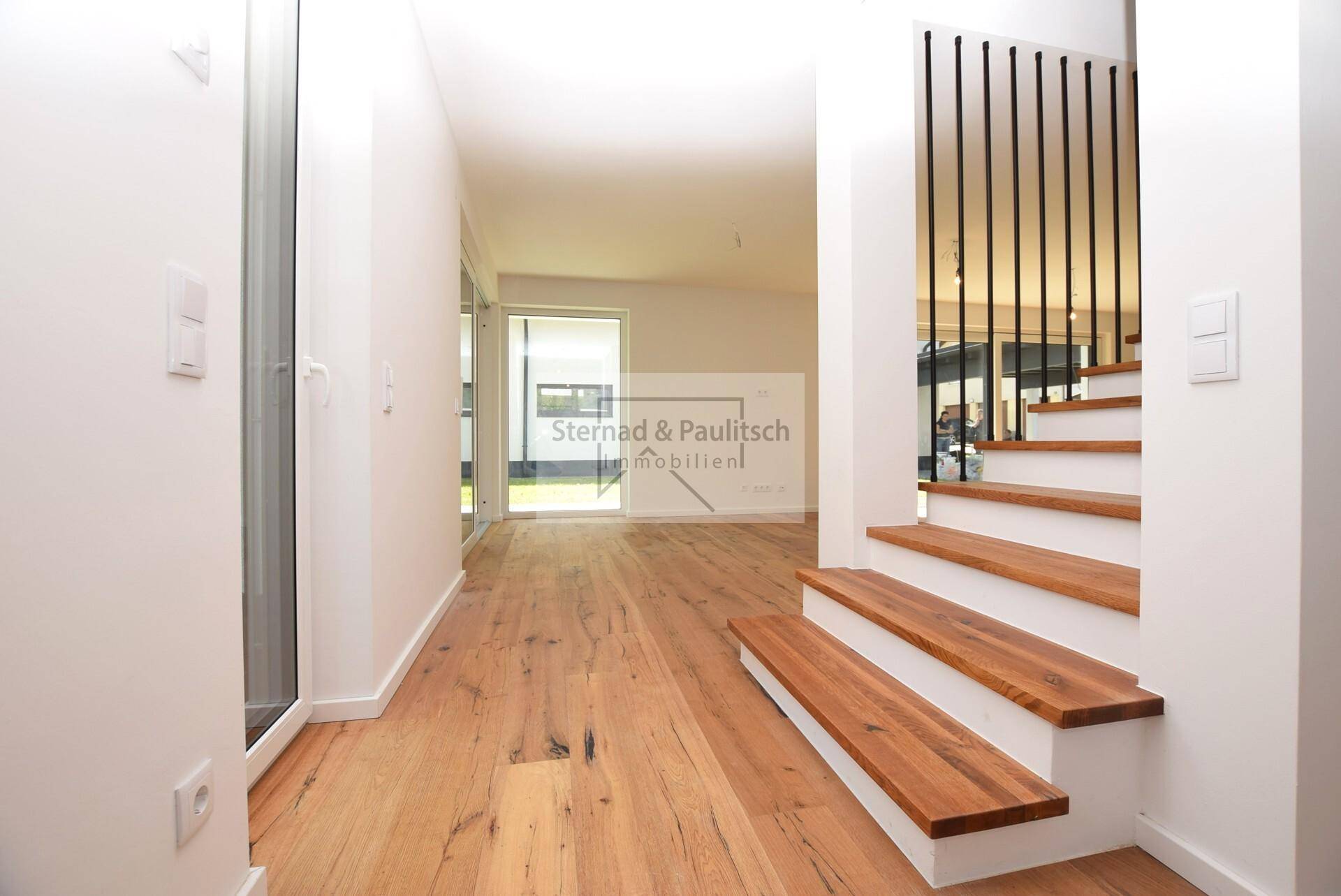 Heller Flur mit Holztreppe, Holzboden und Blick in den offenen Wohnbereich.