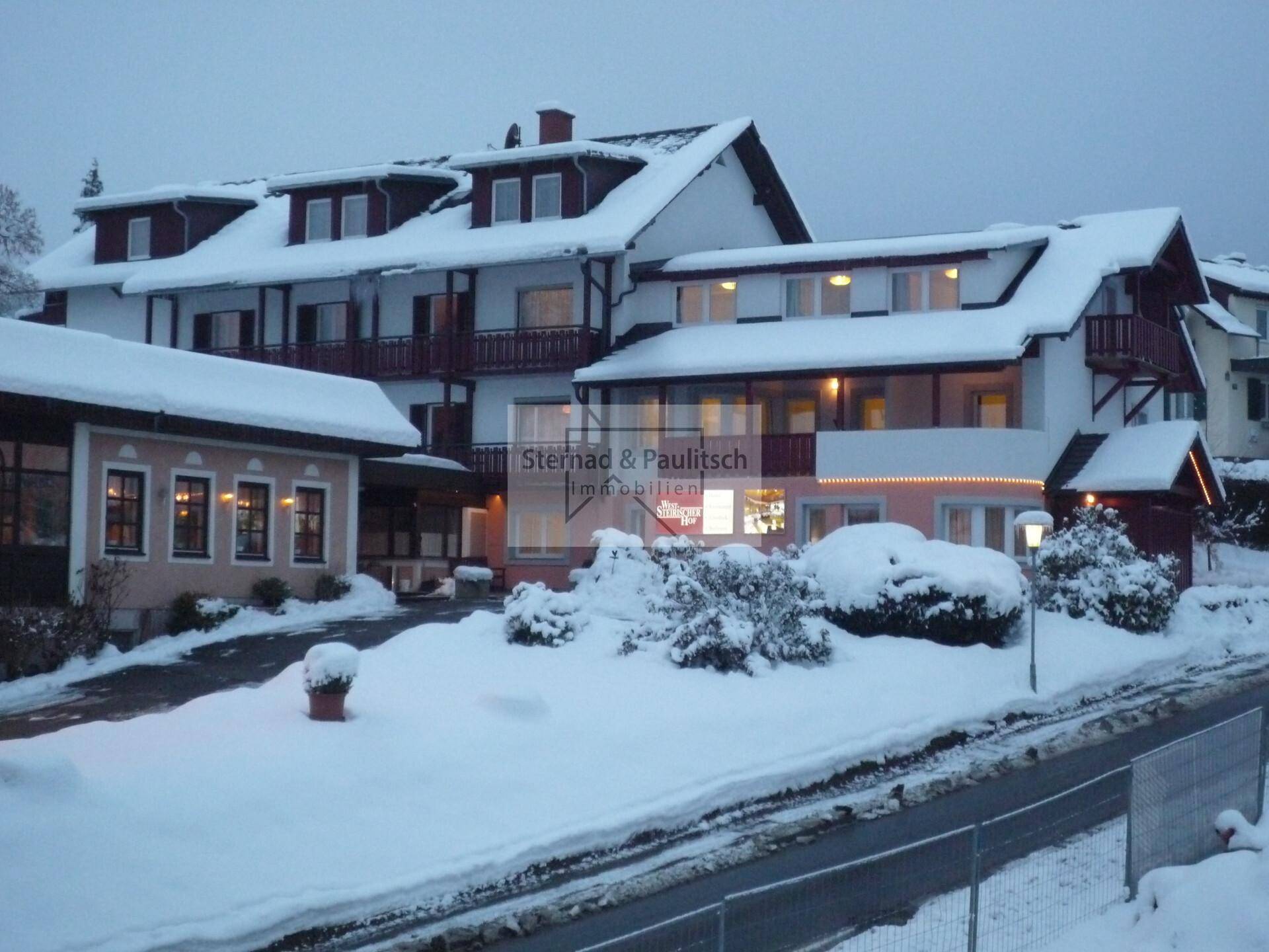 Winterliche Ansicht des Gebäudekomplexes mit verschneiter Landschaft und beleuchteten Fenstern.