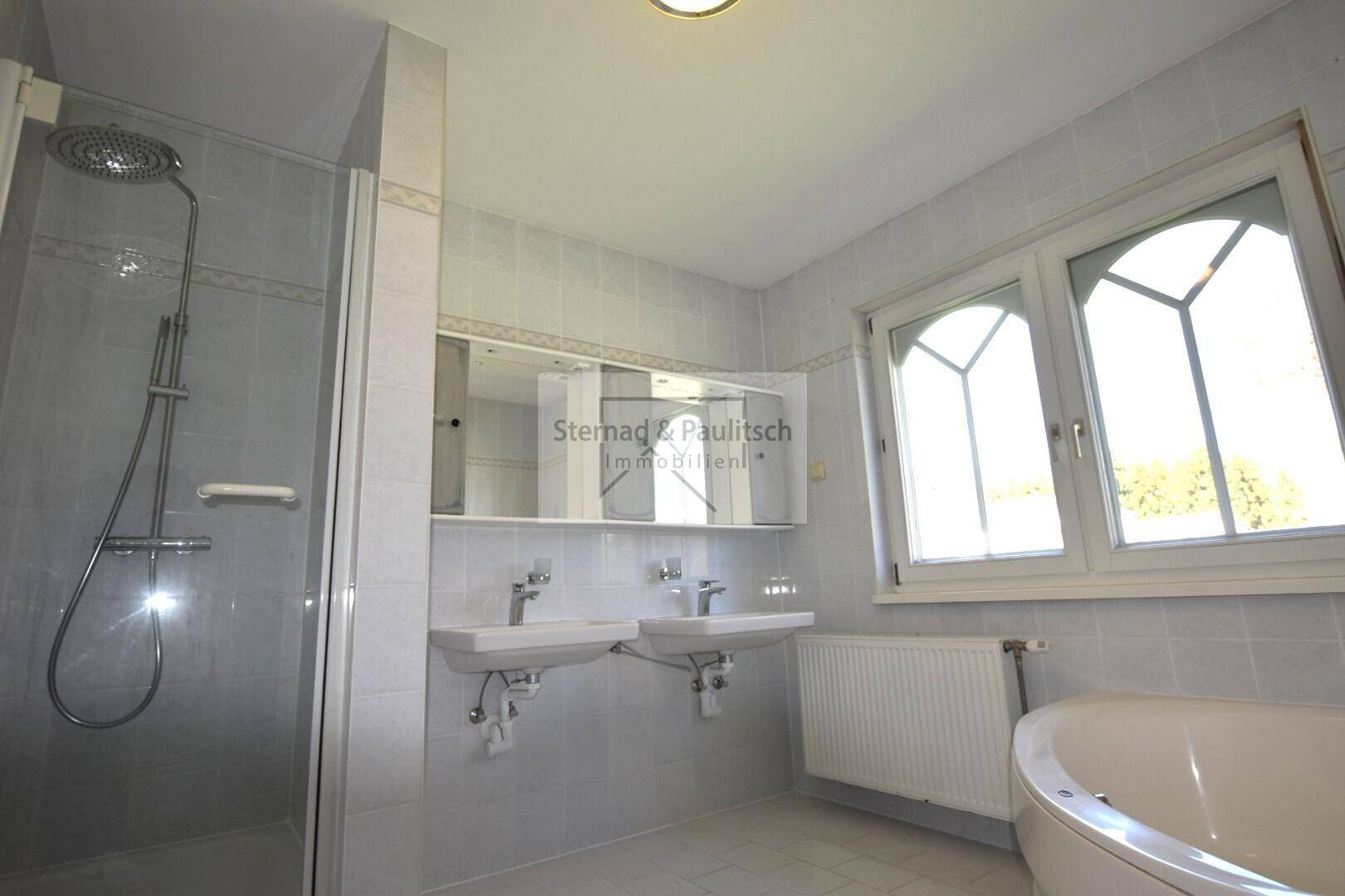 Helles Badezimmer mit Dusche, Doppelwaschbecken und Badewanne, gut beleuchtet durch ein Fenster.