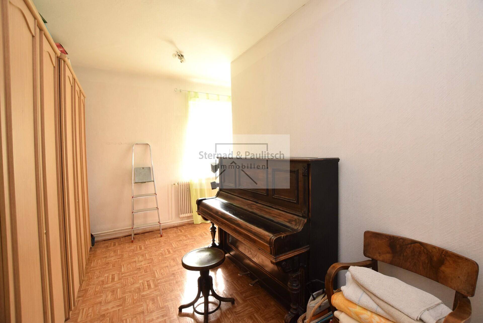 Zimmer mit einem klassischen Klavier, Schränken und Laminatboden.