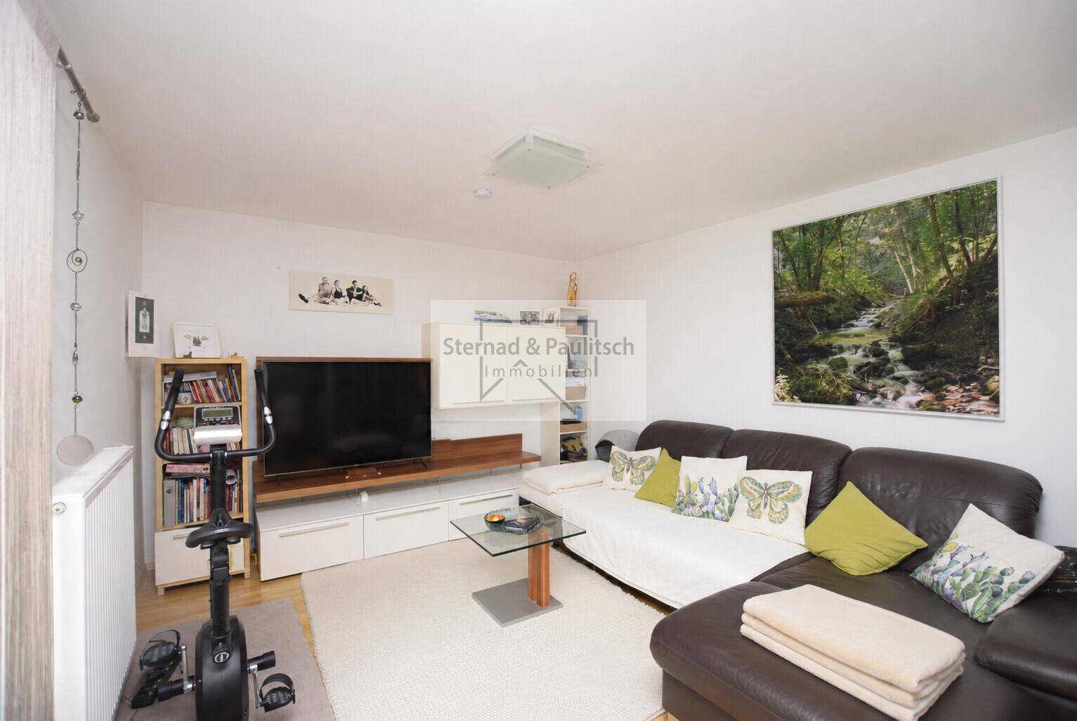 Gemütliches Wohnzimmer mit Sofa, Fernseher und Heimtrainer, ideal für Entspannung und Fitness.