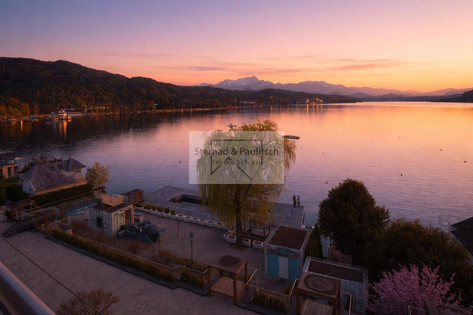 Spektakulärer Sonnenuntergang über dem See mit Blick auf die weitläufige Außenanlage und die Berge.