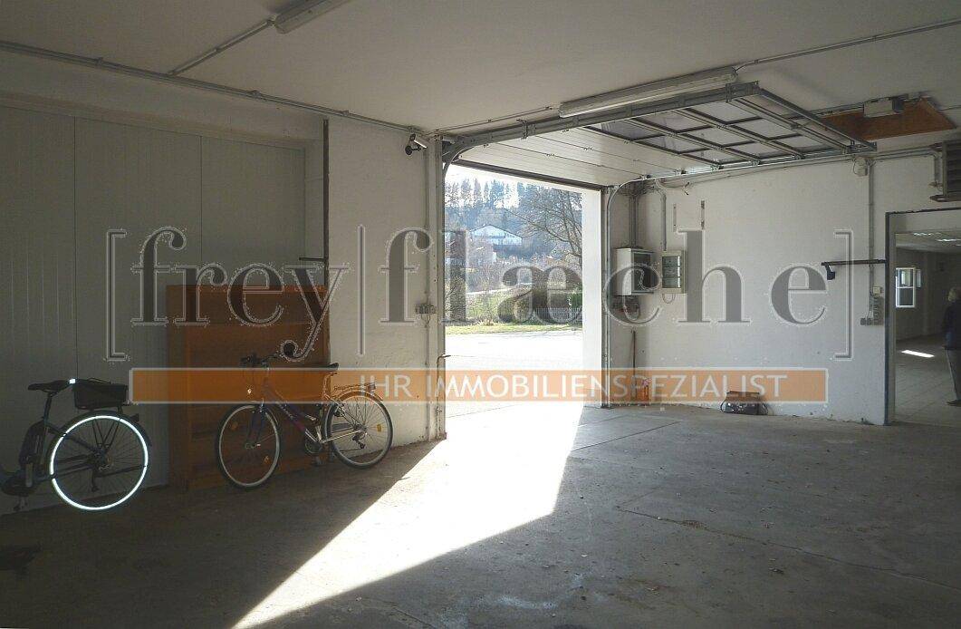 Geräumige Garage oder Werkstatt mit Rolltor, Betonboden und Fahrrädern.