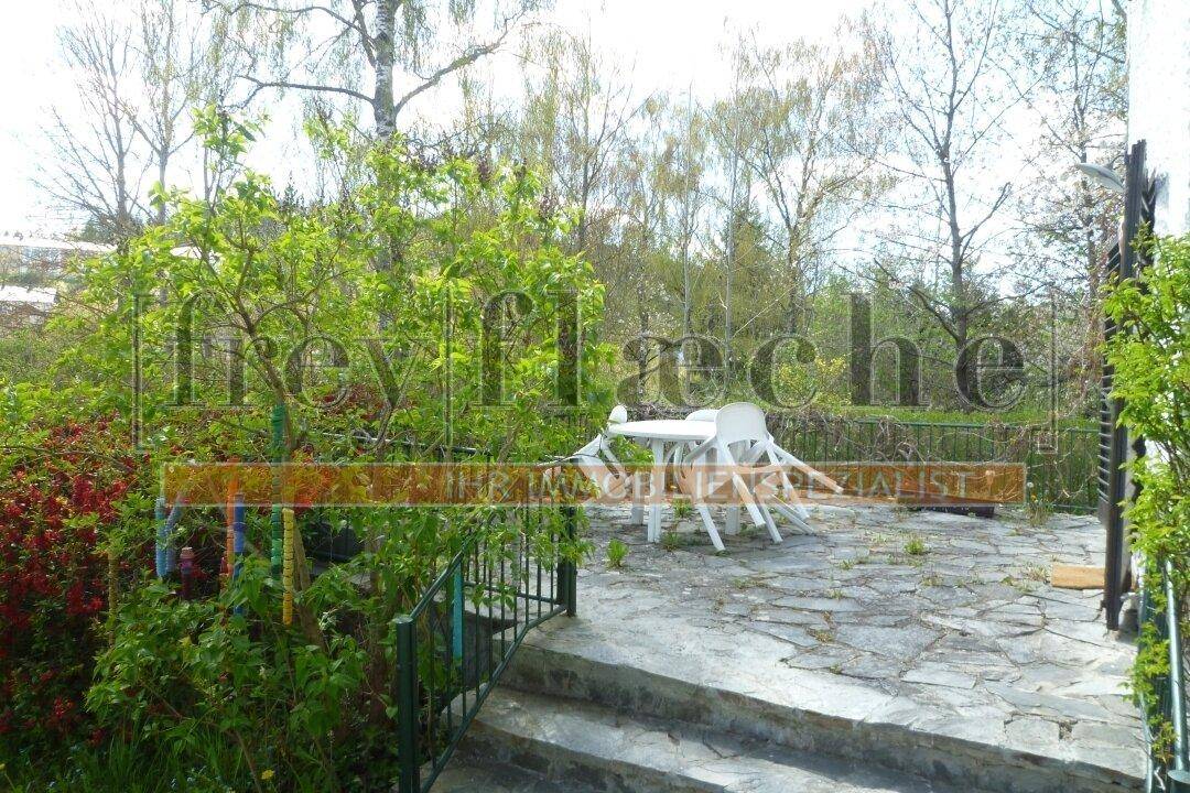 Rustikale Steinterrasse mit Gartenmöbeln, umgeben von üppigem Grün und Bäumen.
