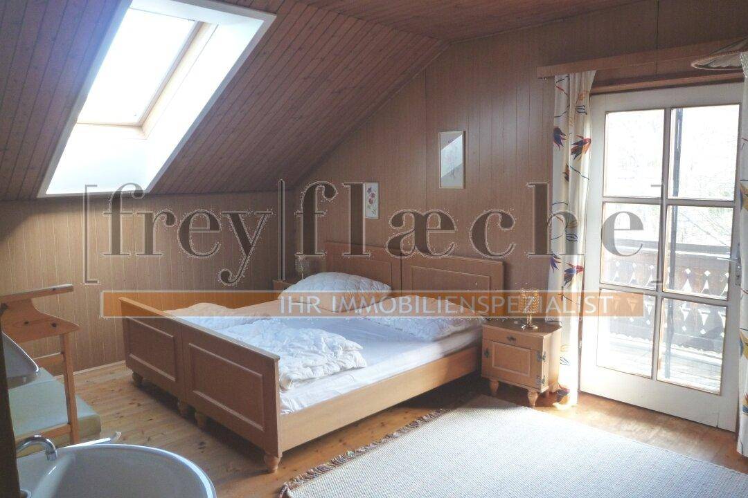 Gemütliches Schlafzimmer im Dachgeschoss mit Holzboden, Dachfenster und Balkonzugang.