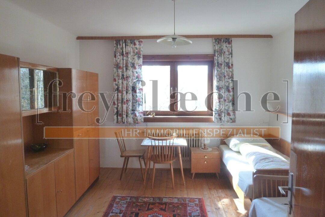 Gemütliches Schlafzimmer mit Einzelbett, Holzschrank und Fenster mit floralen Vorhängen.