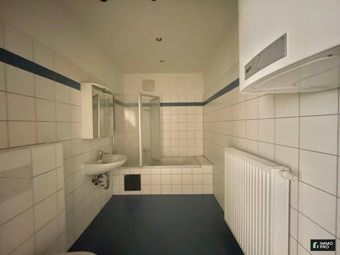 Badezimmer mit weißen Fliesen, blauer Akzentlinie, Dusche und Waschbecken mit Spiegelschrank.