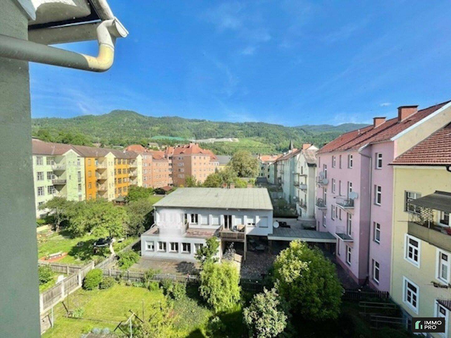 Panoramablick über die Stadt mit bunten Gebäuden, grünen Bäumen und Bergen im Hintergrund.
