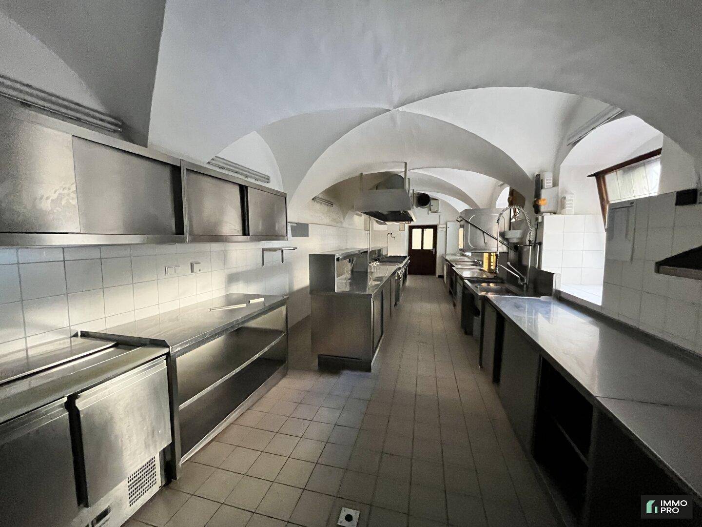Große, professionelle Küche mit Edelstahlgeräten, Fliesenwänden und gewölbter Decke.