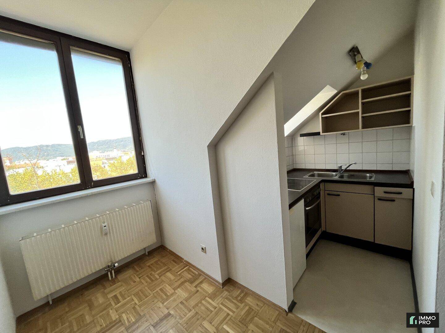 Kleine Küchenzeile im Dachgeschoss mit Fenster, Herd und Spüle, ideal für Singles.