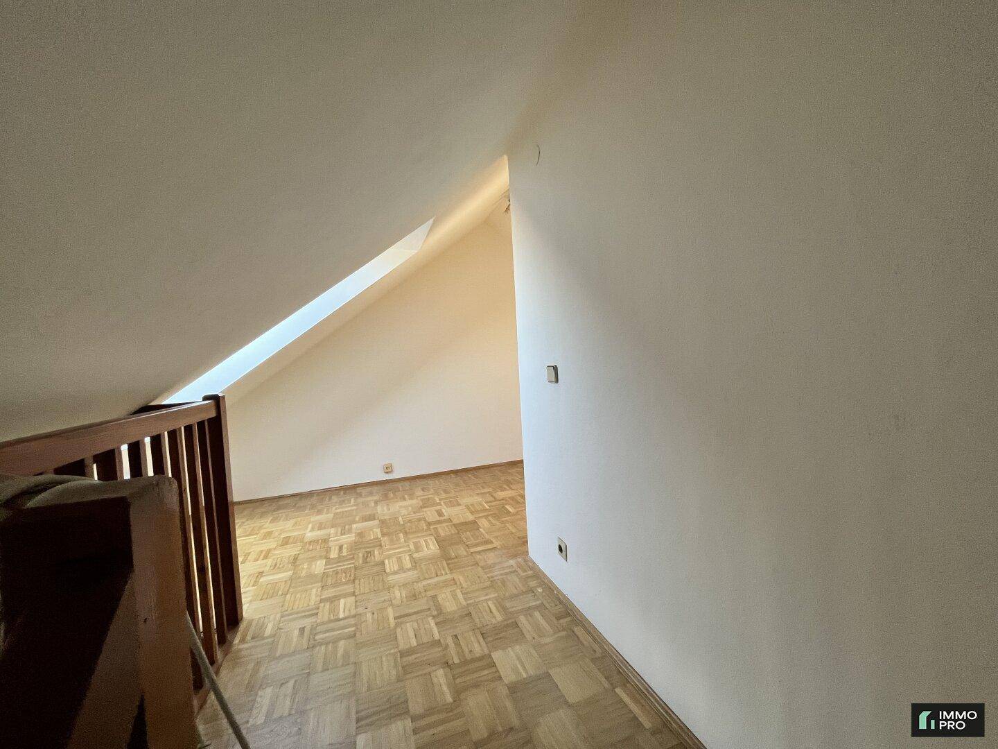 Heller Dachgeschossraum mit Parkettboden, Dachfenster und Holzgeländer.