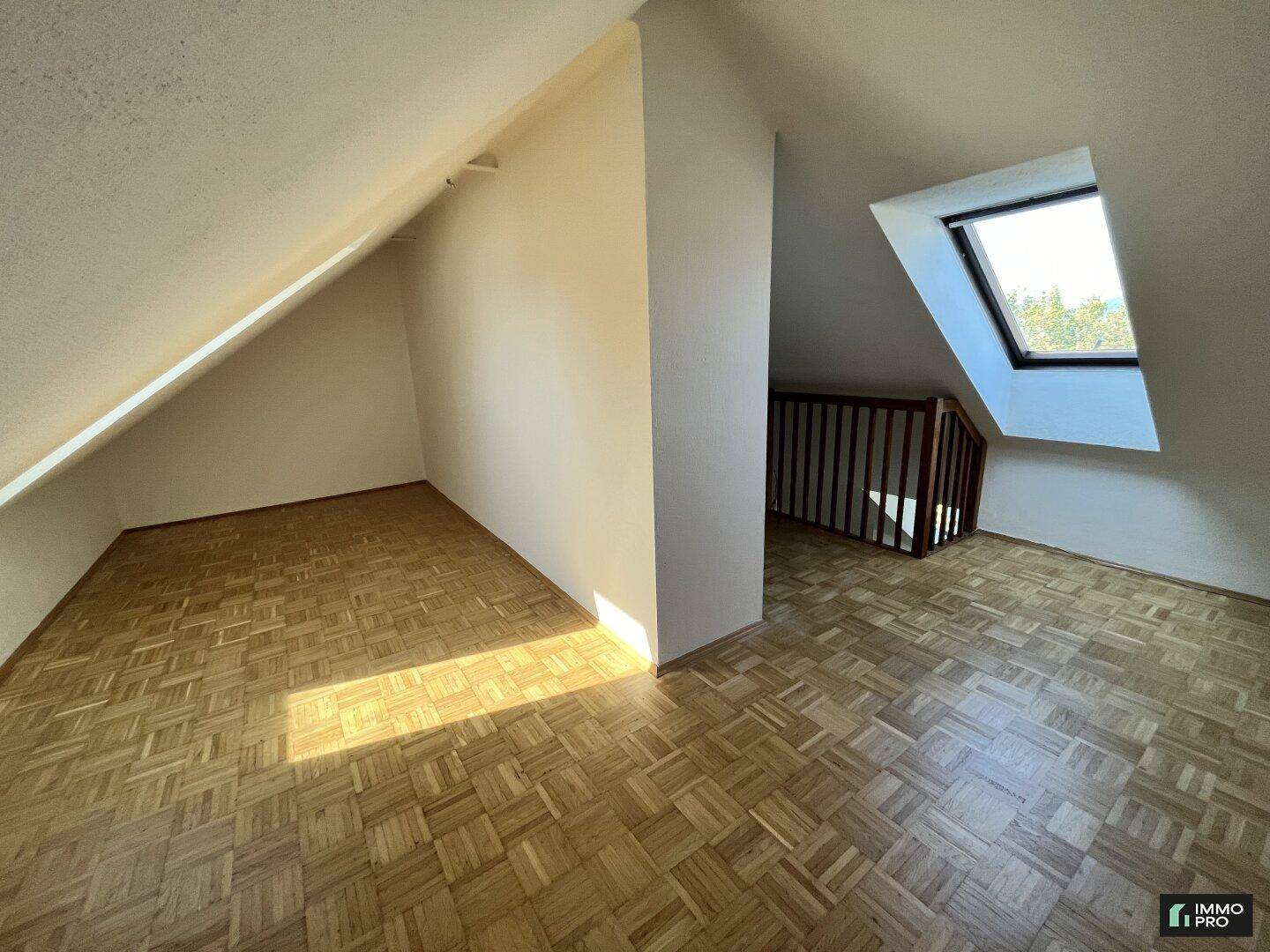 Geräumiger Dachgeschossraum mit Parkettboden, Dachfenster und schrägen Wänden.