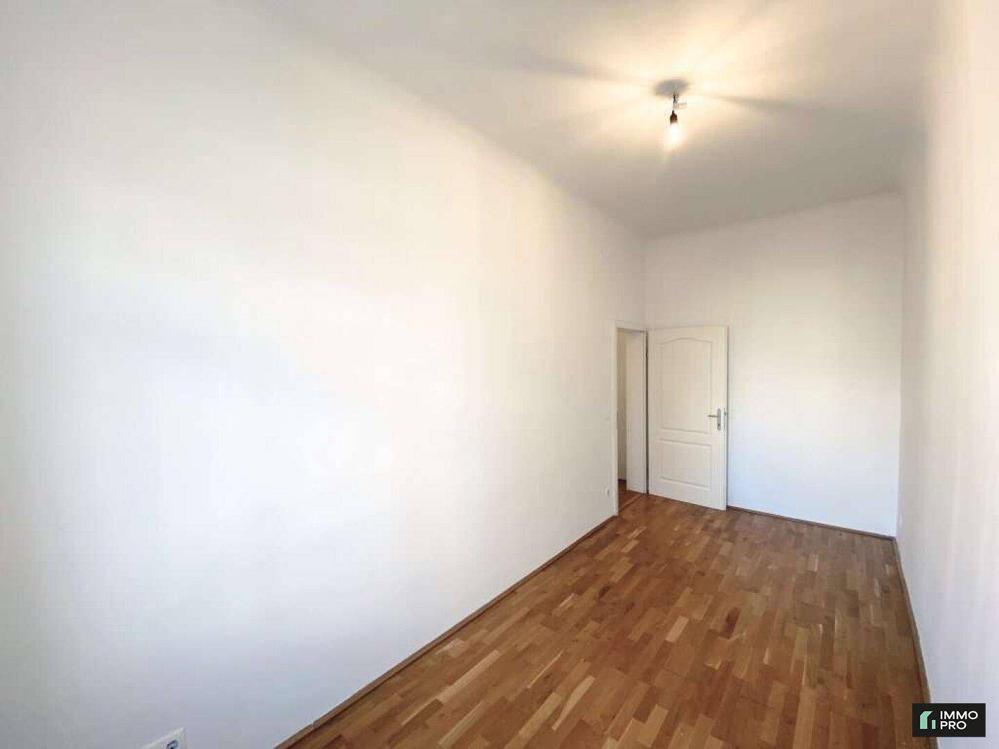 Schlichter Raum mit Holzboden und weiß gestrichenen Wänden, ideal als Schlafzimmer.