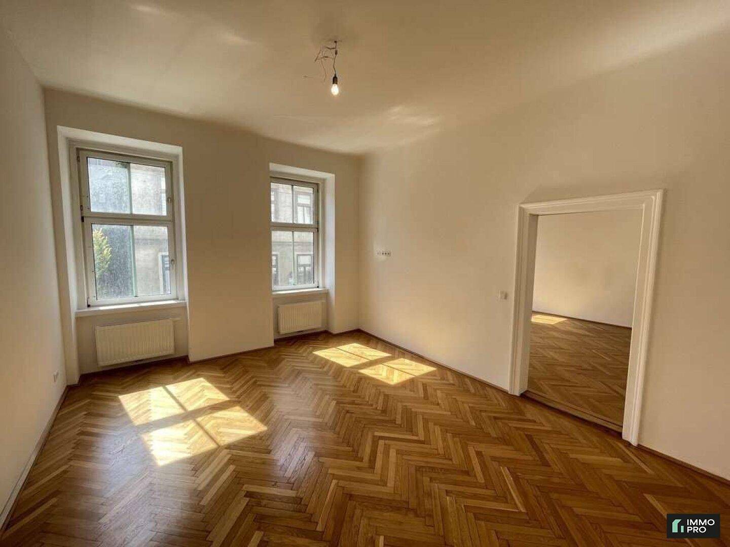 Heller Wohnraum mit Fischgrätparkettboden und großen Fenstern, die viel Tageslicht hereinlassen.